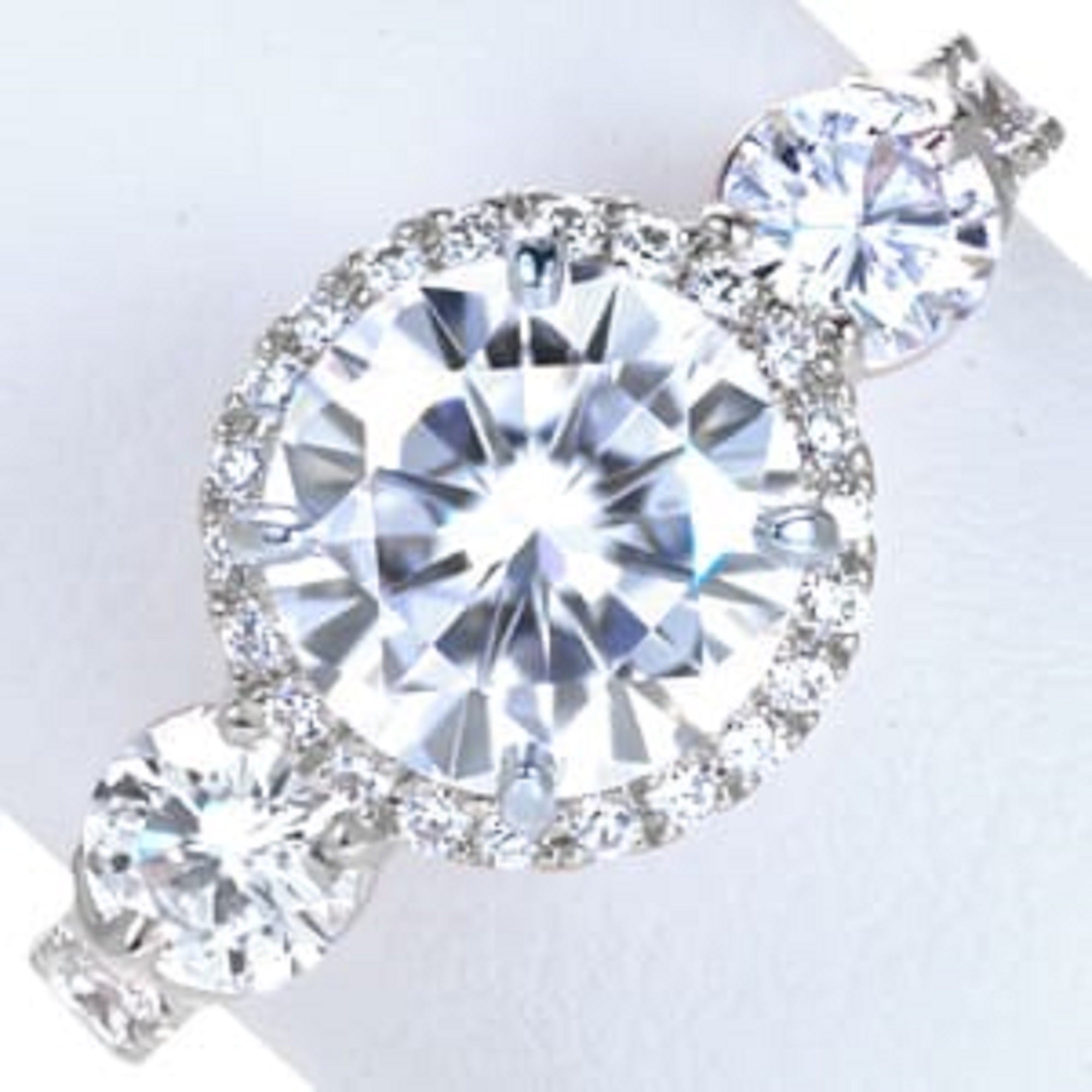 Top view of a 3 carat round lab grown diamond three-stone engagement ring with halo setting and pavé band.