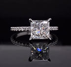 Straight-on view of a square princess cut lab grown diamond ring resting on a reflective dark surface