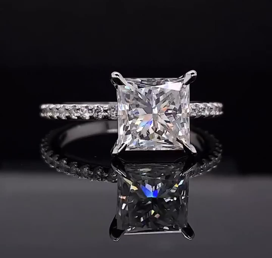 Straight-on view of a square princess cut lab grown diamond ring resting on a reflective dark surface