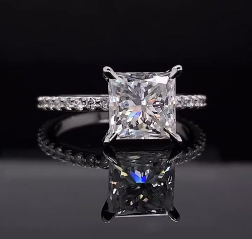 Straight-on view of a square princess cut lab grown diamond ring resting on a reflective dark surface