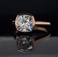 Front view of a 3 carat cushion cut lab grown diamond set in a full gold bezel ring on a black reflective background.