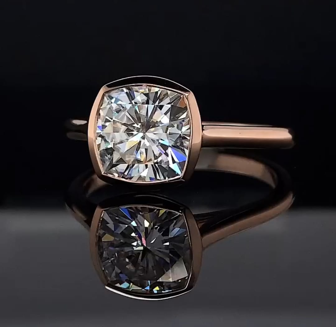 Front view of a 3 carat cushion cut lab grown diamond set in a full gold bezel ring on a black reflective background.