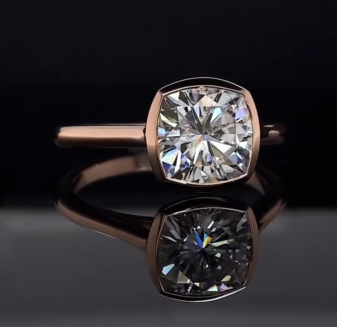 Direct front view of a cushion cut lab grown diamond encircled in a polished gold bezel frame.