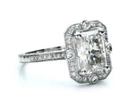 Three-quarter view displaying the radiant cut center diamond and milgrain halo setting on a white background.