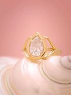 Front view of a 3 carat pear cut lab grown diamond engagement ring in a yellow gold hybrid bezel setting resting on a seashell