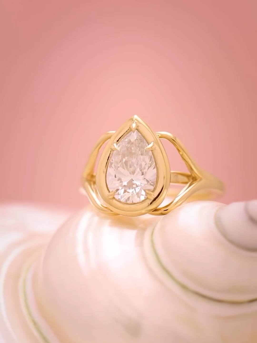Front view of a 3 carat pear cut lab grown diamond engagement ring in a yellow gold hybrid bezel setting resting on a seashell