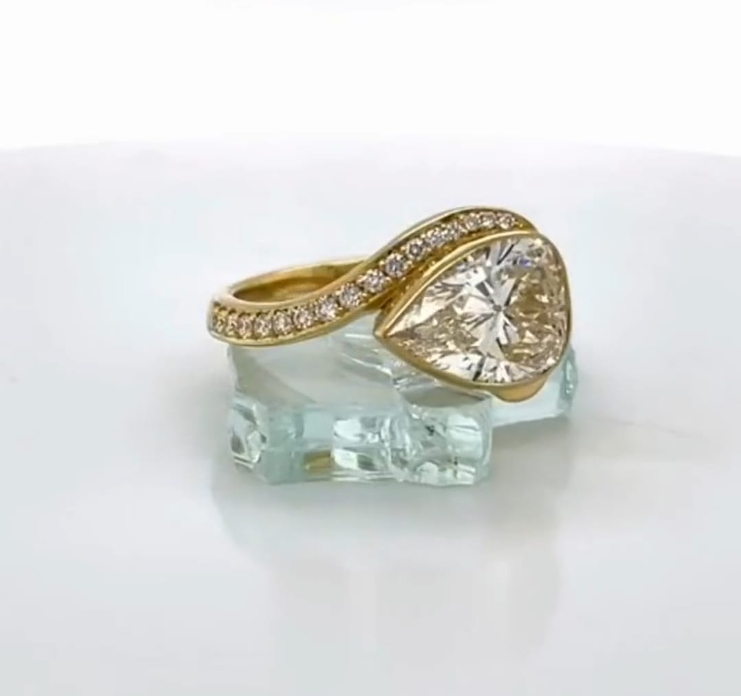 Angled shot showing the asymmetrical pave diamond band sweeping around a 3 carat pear diamond