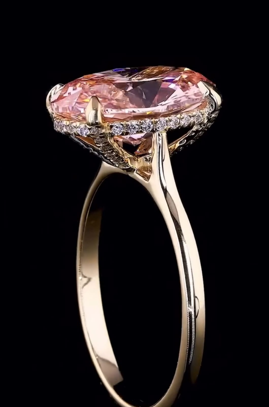Side profile view of a 3 carat fancy pink oval lab grown diamond engagement ring with a micro pave hidden halo in yellow gold