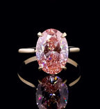 Top down view of a vibrant 3 carat fancy pink oval lab diamond ring on a black reflective background
