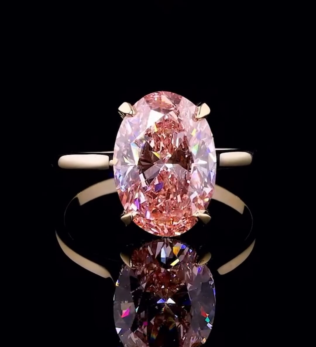 Top down view of a vibrant 3 carat fancy pink oval lab diamond ring on a black reflective background