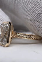 Side view of a 5 carat radiant cut lab grown diamond ring in a gold bezel setting with a chevron engraved band
