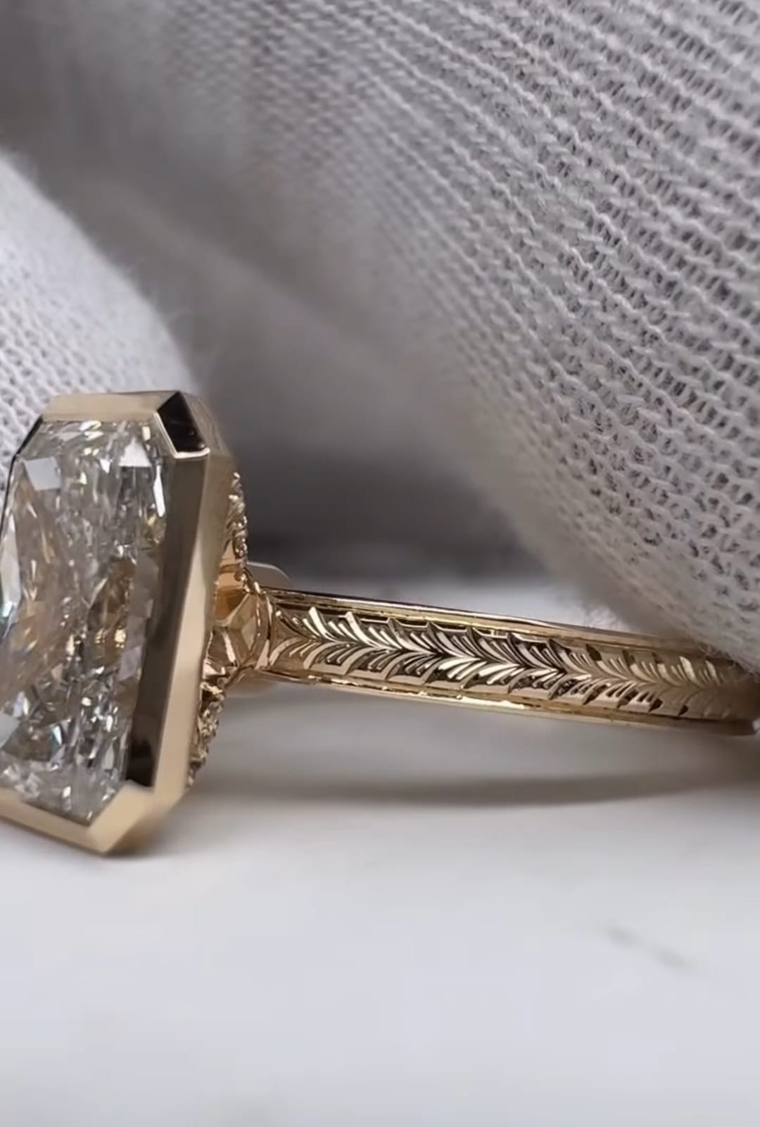 Side view of a 5 carat radiant cut lab grown diamond ring in a gold bezel setting with a chevron engraved band