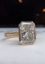 Angled view of a 5 CT radiant cut lab diamond ring set in a full yellow gold bezel on a white surface
