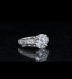 Angled shot displaying a 3 carat round brilliant lab diamond with side accent diamonds on an engraved white gold band