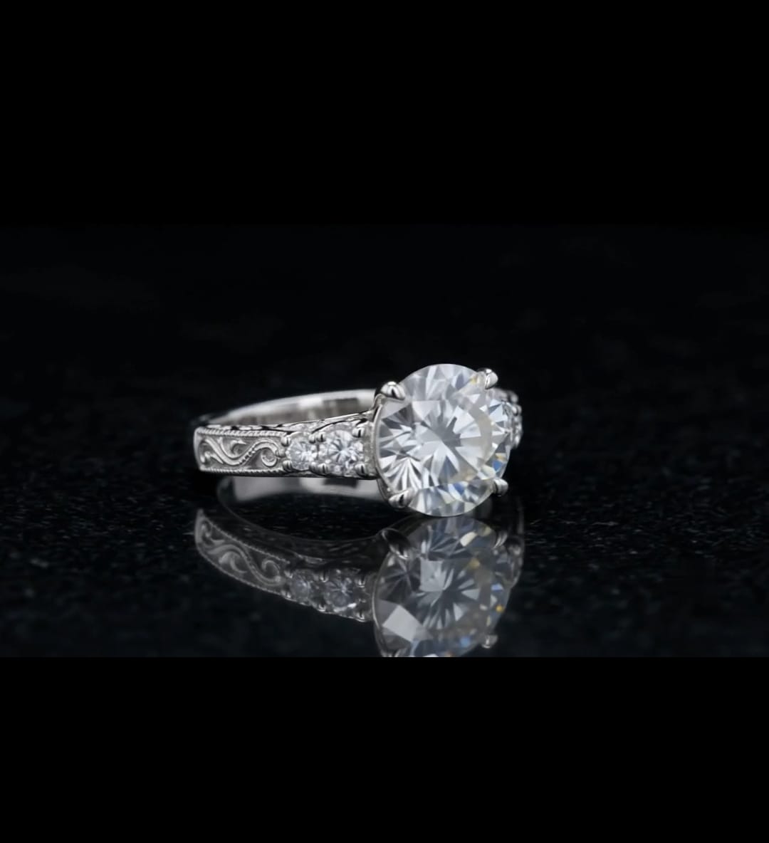 Angled shot displaying a 3 carat round brilliant lab diamond with side accent diamonds on an engraved white gold band