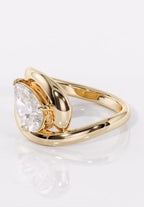 Side view showing the prong-secured pear cut diamond nestling inside a fluid yellow gold swirl setting