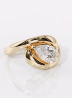 Top-down view of a 2 carat pear cut lab grown diamond surrounded by an organic yellow gold bypass curve