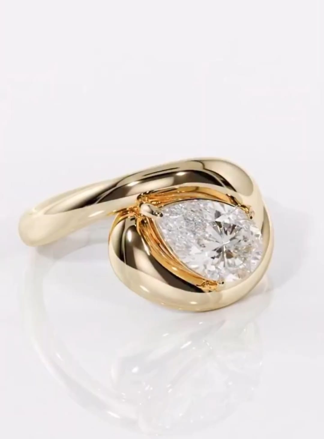 Top-down view of a 2 carat pear cut lab grown diamond surrounded by an organic yellow gold bypass curve