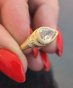 Close-up view of a vintage style yellow gold engagement ring featuring hand-engraved patterns and side diamond accents