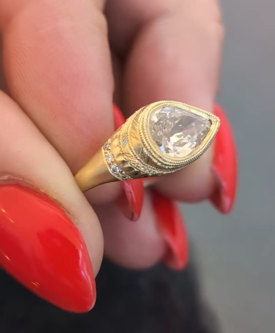 Close-up view of a vintage style yellow gold engagement ring featuring hand-engraved patterns and side diamond accents