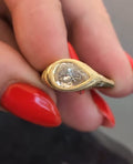 Horizontal perspective of a 2 carat pear cut diamond in a milgrain bezel setting with detailed yellow gold band