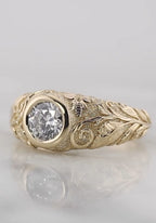 Angled studio shot of a 2 carat round lab grown diamond bezel ring featuring hand-engraved leaf patterns and a bee motif on yellow gold