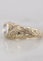 Side view highlighting the detailed hand-carved leaf scrollwork and textured background on a yellow gold engagement ring