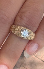 On-finger view of a 2 carat round lab grown diamond ring with a wide hand-engraved botanical yellow gold band