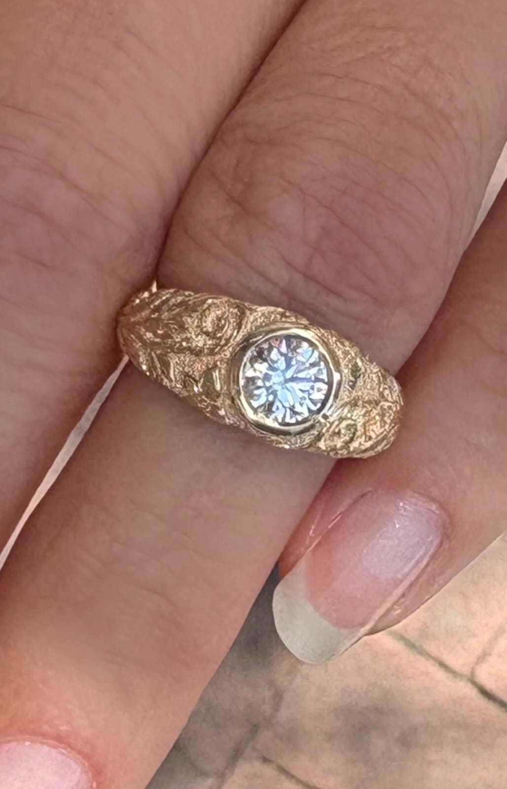 On-finger view of a 2 carat round lab grown diamond ring with a wide hand-engraved botanical yellow gold band