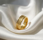 Close up view of a men's yellow gold chevron engraved band resting on white silk background