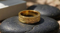 Horizontal side view of men's gold chevron ring with milgrain trim resting on a smooth stone