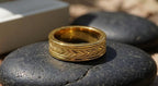 Horizontal side view of men's gold chevron ring with milgrain trim resting on a smooth stone
