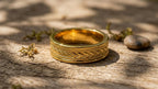 Natural sunlight shot showing detail of men's engraved chevron gold band on a wooden surface