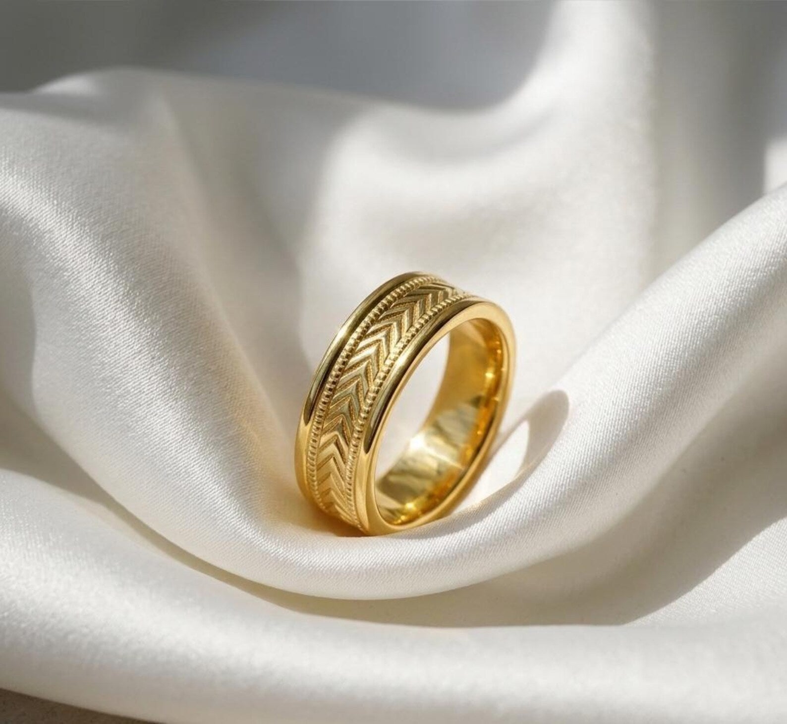 Studio shot of a men's yellow gold band featuring herringbone engraving and polished edges