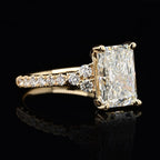 Angled side view showing radiant cut diamond and pavé set round accent diamonds on a yellow gold band