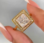Close up view of a 3CT princess cut lab diamond held up in a square pavé halo yellow gold setting
