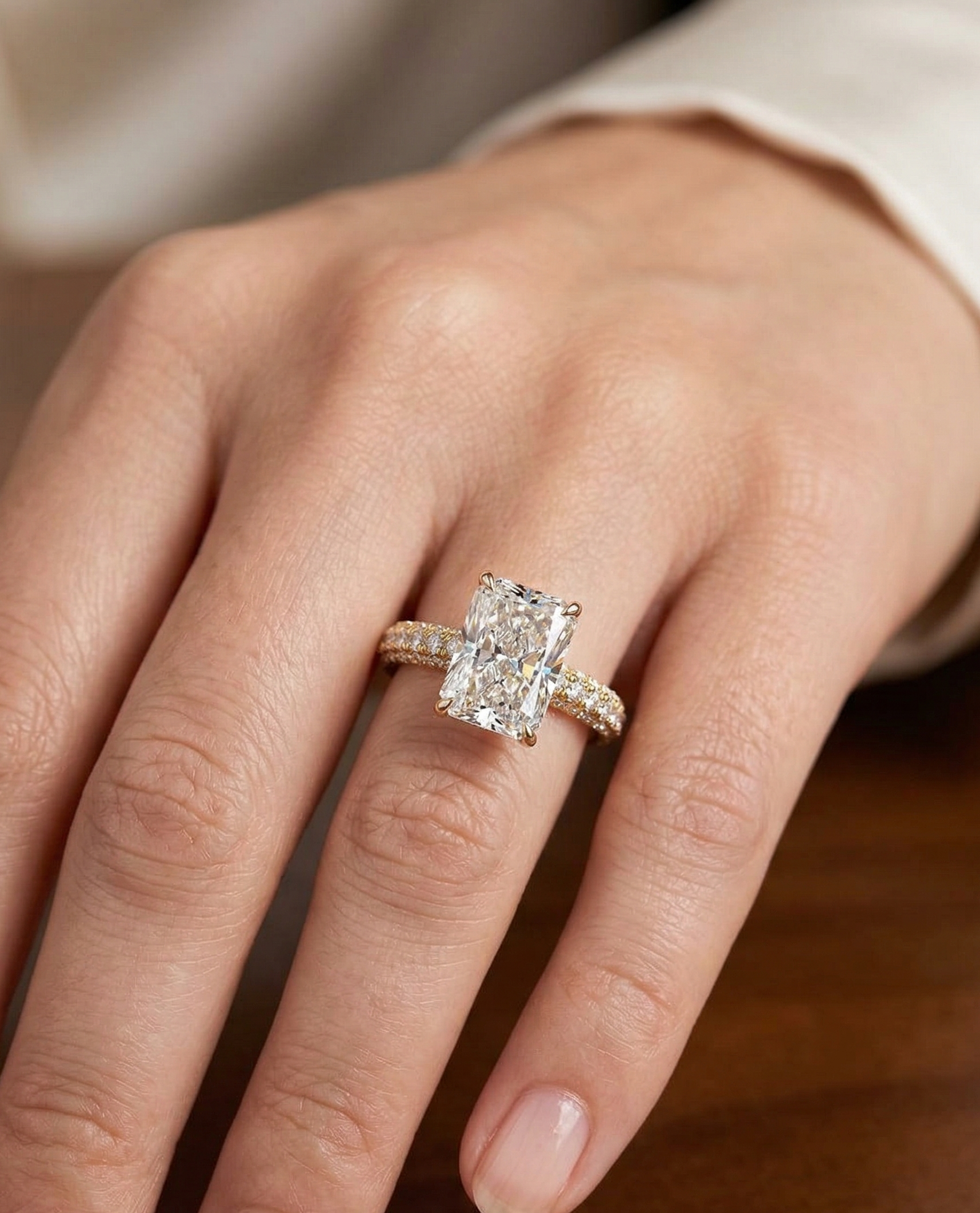 Top view on finger showing a 3 carat elongated radiant cut lab diamond engagement ring on a multi-row pavé yellow gold band