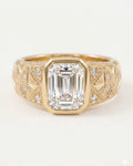 Front view of a yellow gold engagement ring featuring a large bezel-set emerald cut diamond on a wide, engraved band.