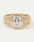 Front view of a yellow gold engagement ring featuring a large bezel-set emerald cut diamond on a wide, engraved band.