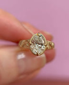 Top view showing a 3 carat oval lab grown diamond framed in a milgrain bezel setting in yellow gold