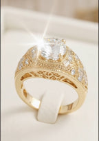 Top-down view of an Art Deco inspired gold statement ring showcasing a brilliant round-cut center stone set in a milgrain-bordered, wide filigree band with accent diamonds.