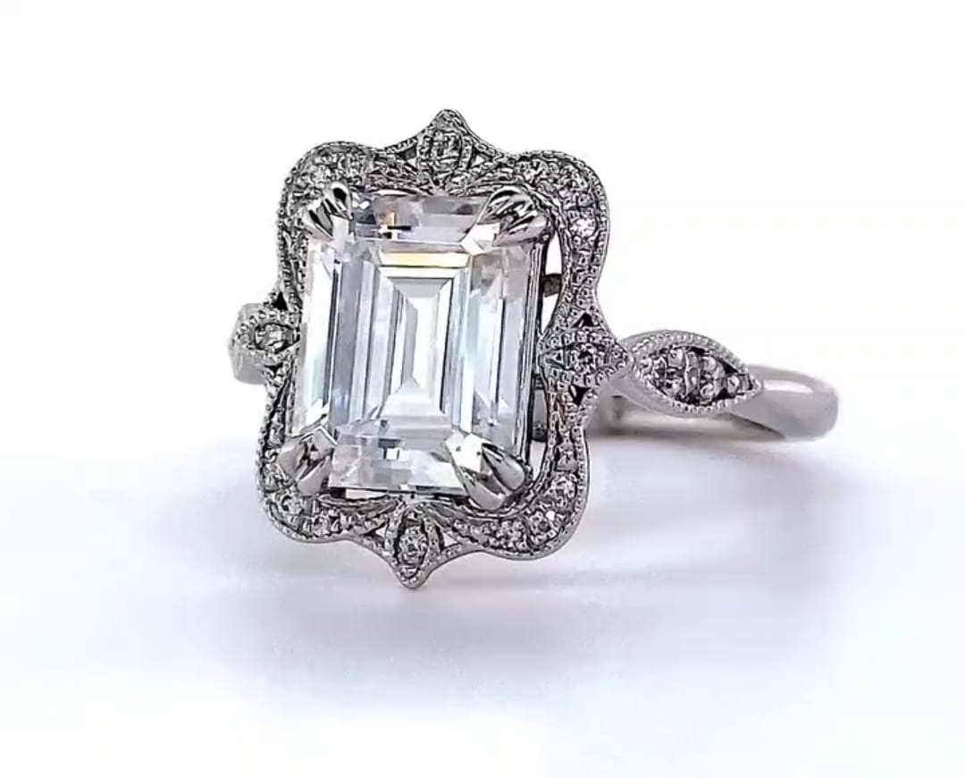 Direct top-down view displaying the step cuts of a 3 CT emerald lab diamond in a vintage scalloped halo.