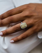 Top-down hand view highlighting the inner yellow diamond halo and outer white diamond halo around a 2 CT radiant center stone.