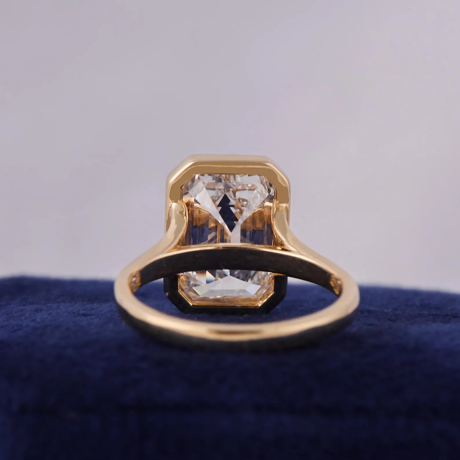 Inner band and under-gallery view of a 3 CT emerald cut lab grown diamond ring in a yellow gold bezel setting.