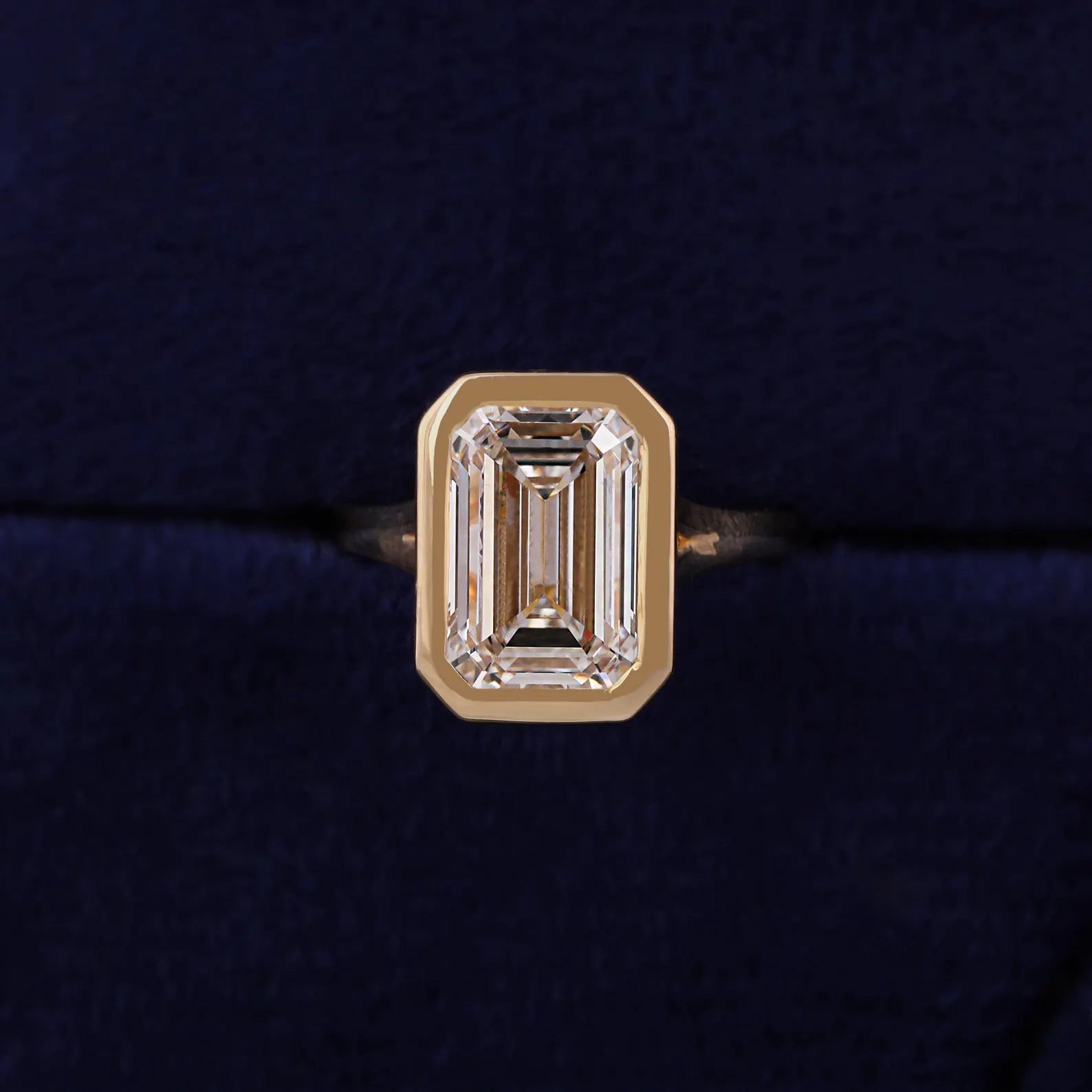 Top-down view highlighting step-cut facets of a 3 CT emerald lab diamond inside a solid gold full bezel frame.