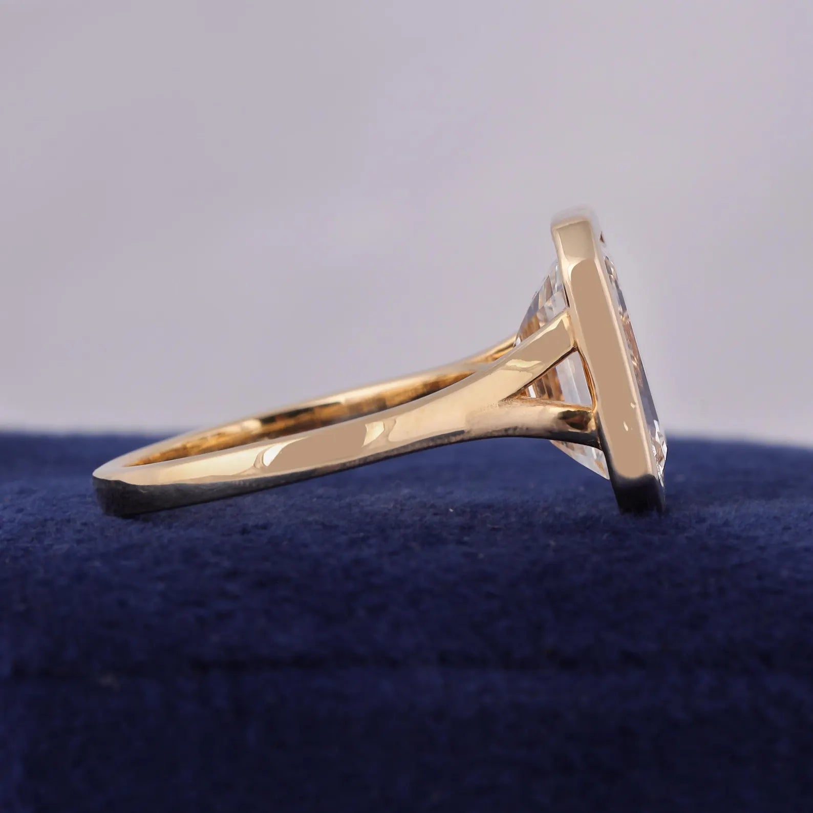 Side angle view highlighting the sleek yellow gold bezel and clear step-cut diamond facets.