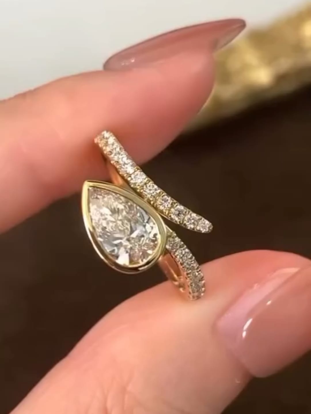 Top angle view highlighting the brilliant-cut pear lab diamond encased in a gold bezel with delicate pavé band details.