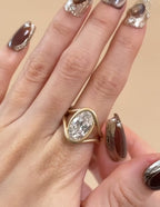 On-hand view of a 3 carat oval lab grown diamond engagement ring with matte yellow gold swirl bezel setting