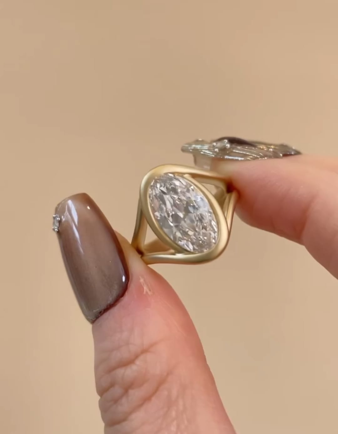 Close-up held shot showing the fluid wave-like bezel setting of a 3 ct oval lab diamond ring in matte gold