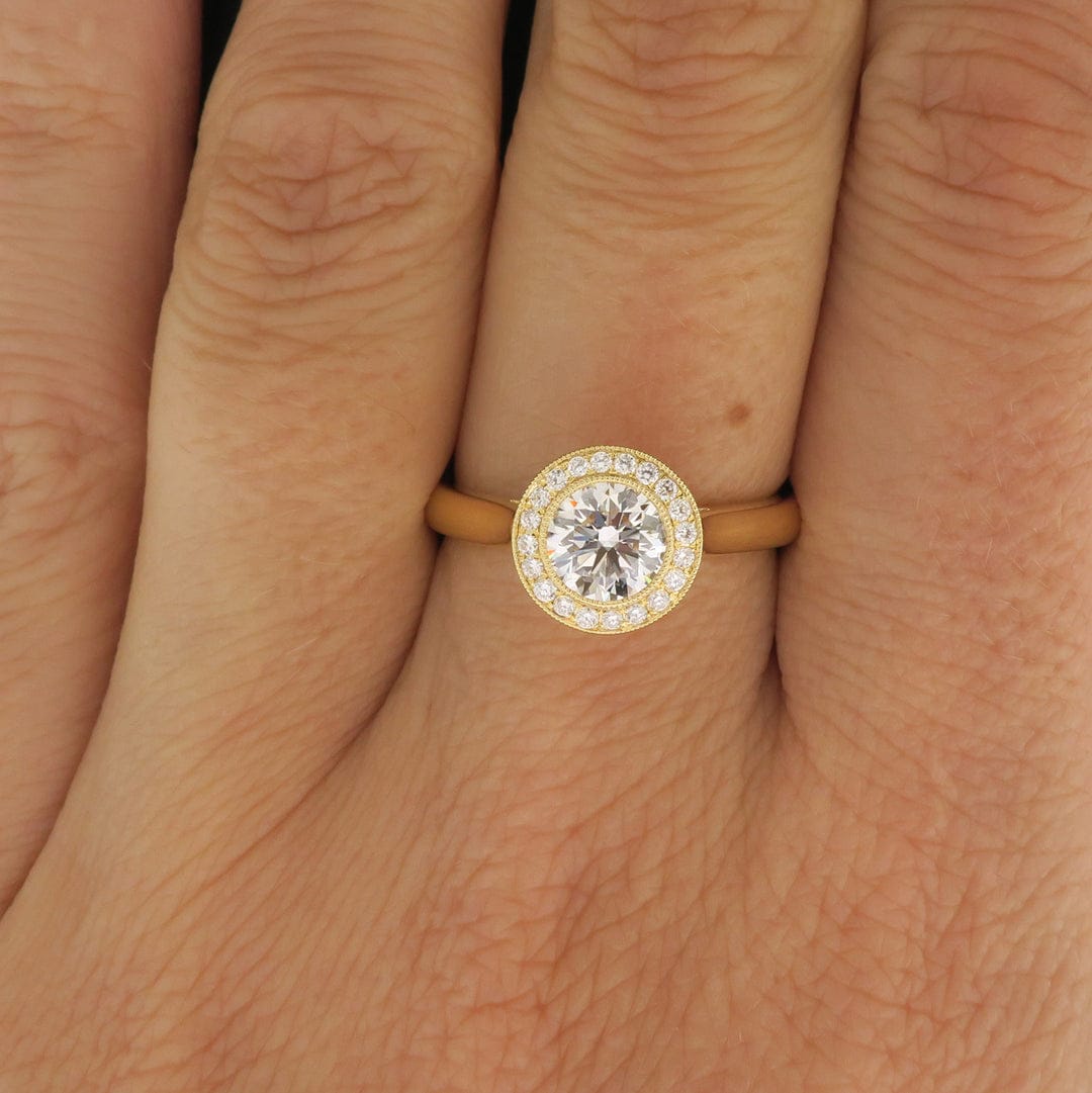 Top-down view on hand of a 2 carat round lab grown diamond ring with yellow gold milgrain halo setting